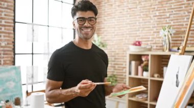 Parlak bir sanat stüdyosunda resim yapan, siyah gömlek ve gözlük takan neşeli, genç bir İspanyol..