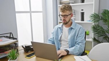 Modern ofis odasında dizüstü bilgisayarla çalışırken sakallı ve gözlüklü yakışıklı genç adam öksürüyor..