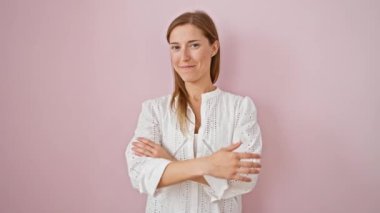 Neşeli genç bir kadın kendine güvenen bir poz verir, kollarını kavuşturur, pozitiflik saçar. Çekici bir kadın kameraya bakarak dostça bir gülümseme sergiliyor. Serin pembe bir arkaplanda izole edilmiş.