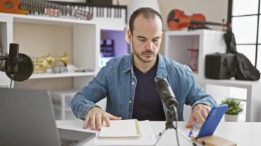 Evde müzik stüdyosunda mikrofon ve dizüstü bilgisayarla çalışan sakallı kel bir adam.