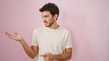 Yakışıklı, sakallı genç bir adam pembe izole bir arka plan sunuyor..