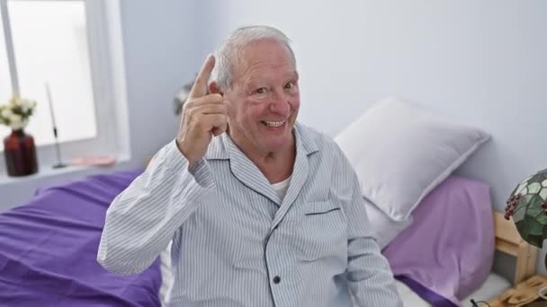 一个快乐的老人 坐在卧室里 聪明地用一个明亮的 尤里卡 指了指一个手指 成功的时刻 当穿着睡衣在家里 — 图库视频影像