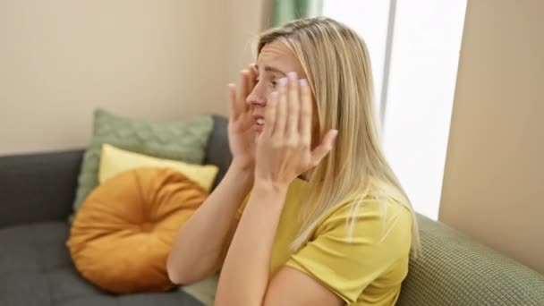 年轻的金发女人穿着T恤衫 双手沾满了脸 忧郁和忧伤 在家里烦恼和烦躁 — 图库视频影像