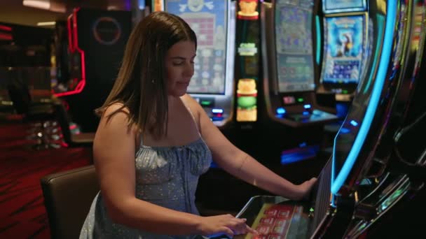 活発なカジノの設定でスロットマシンをプレイしながら微笑んでいる若いブルネットの女性 — ストック動画