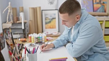 Sanat malzemeleriyle çevrili yaratıcı bir stüdyoda resim çizen odaklı genç bir adam.
