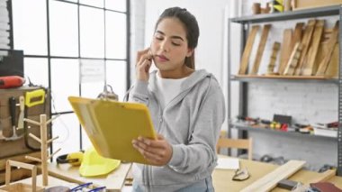 Bir marangoz atölyesinde günlük kapüşonlu bir kapüşonlu İspanyol kadın telefonda konuşurken planlarını inceliyor..