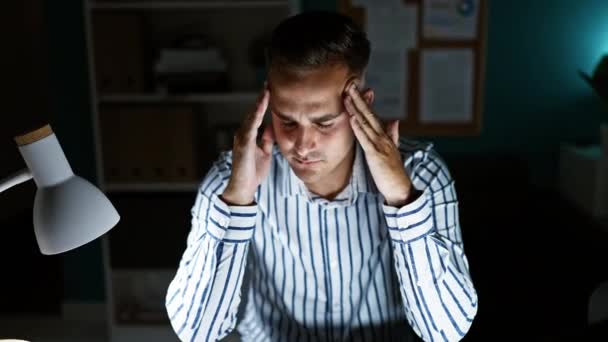 ストライプシャツの思慮深い男性は デスクランプで照らされたオフィスの設定でストレスを示しています — ストック動画