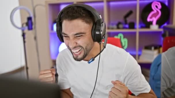 一个快乐的男人带着耳机 在一个现代化的霓虹灯照明的房间里庆祝着游戏的胜利 — 图库视频影像