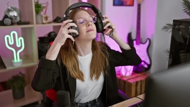 ヘッドフォンを持つ若い女性は 夜のネオンライトゲームルームでコンピュータで働いています — ストック動画