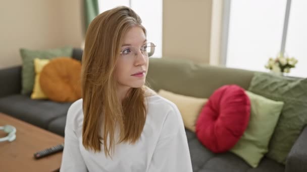 Kontemplacyjna Młoda Blondynka Okularach Siedzi Domu Kanapie Tworząc Pogodną Scenę — Wideo stockowe