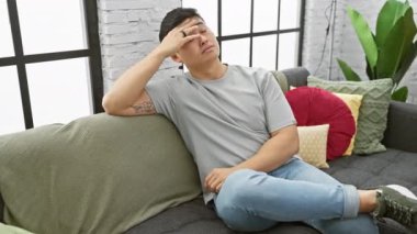 Rahat Asyalı bir adam modern bir oturma odasında, rahat ve rahat bir şekilde bir koltuğa oturur..