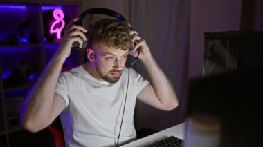 Kulaklık takan beyaz sakallı genç bir adam neon ışıklı bir oyun odasında gülüyor..