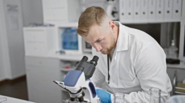 Modern bir laboratuvar ortamında mikroskopla örnekleri analiz eden odaklanmış genç bir adam..