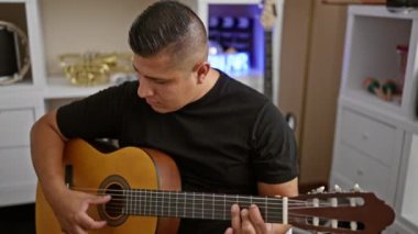 Yakışıklı genç Latin adam klasik gitar çalarak kulübün samimi müzik stüdyosunun atmosferinde melodi büyüsü yaratıyor.