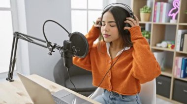 Genç bir İspanyol kadın müzik stüdyosunda kulaklıkları ve dizüstü bilgisayarıyla şarkı söylemekten hoşlanıyor..