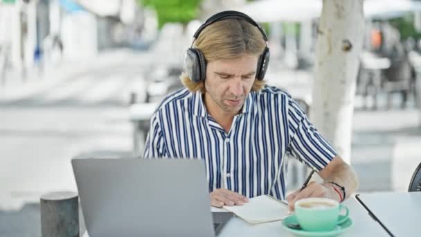 Kulaklıklı Bir Adam Şehirdeki Bir Kafede Dizüstü Bilgisayar Kullanıyor Yanında — Stok video