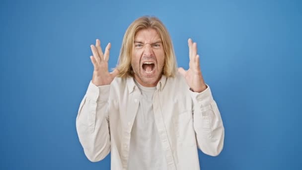 一个灰心丧气的男人 留着一头长长的金发 穿着一件休闲衫 对一个孤立的蓝色背景表示愤怒 — 图库视频影像