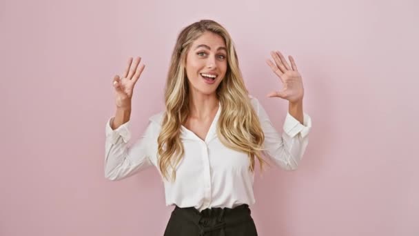 自信を持って幸せなブロンドの若い女性シャツを指し示すと笑顔で ピンクの孤立した背景に彼女の指で8番をジェスチャー — ストック動画