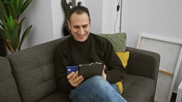 在舒适的客厅里 一个拿着平板电脑和信用卡躺在沙发上的男人笑着 表达着快乐的经济承诺 — 图库视频影像