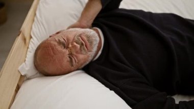 Yetişkin bir adam acı içinde yatağında yatıyor. Rahatsızlıktan suratını buruşturuyor. Sağlık hizmetlerini ya da yaşlıları tasvir ediyor..