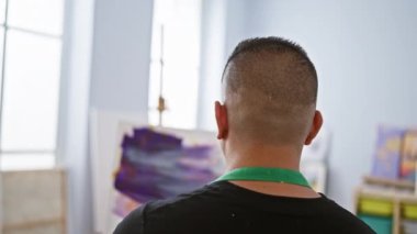 Tutkulu genç Latin ressam, elinde fırçayla, resim sehpası üzerine resim çiziyor, yaratıcılığın akışına hevesle hazır..