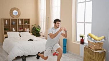 Yatak odasında ağırlıklarla egzersiz yapan genç bir adam ev ortamında sağlıklı bir yaşam tarzı sergiliyor..