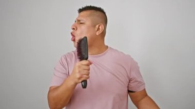 Yakışıklı genç Latin adam sevinçle şarkı söylüyor, mikrofon olarak fırçayı kullanıyor, beyaz bir arka planda izole edilmiş.