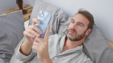 Yatak odasında akıllı telefon kullanan sakallı adam, günlük hayattaki teknolojiyi yansıtıyor..