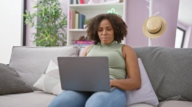 Kanepede dizüstü bilgisayar kullanan Afrikalı Amerikalı bir kadın.