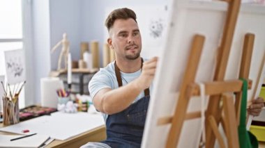 Sakallı, gülümseyen bir adam, parlak bir sanat stüdyosundaki tuvale resim çizer, yaratıcılığı ve öğrenmeyi tasvir eder..
