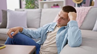 Genç İspanyol bir adam, rahat bir oturma odasındaki kanepede düşünceli bir şekilde oturuyor, elinde akıllı bir telefon tutuyor.