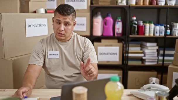Joven Voluntario Latino Recibiendo Videollamadas Tomando Notas Centro Caridad — Vídeo de stock