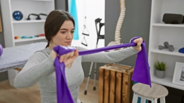 Сфокусированная Молодая Женщина Использует Фиолетовую Ленту Сопротивления Тренировок Современной Клинике — стоковое видео
