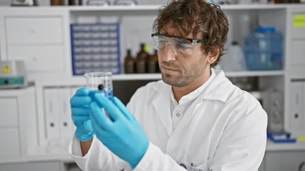 グラスとひげのある笑顔の科学者は 実験室の設定で手袋を着用しながらテストチューブを検査する — ストック動画