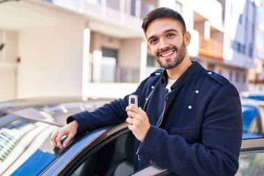 Young hispanic man smiling confident holding key of new car at street