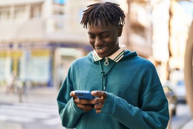 Sokakta akıllı telefon kullanan, kendinden emin gülümseyen Afrikalı Amerikalı bir adam.