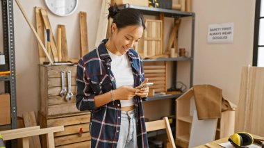 İyi organize edilmiş bir marangoz atölyesinde genç bir Asyalı kadın telefonuyla mesajlaşırken gülümsüyor..