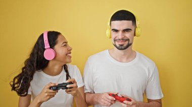 Gülümseyen güzel çift, kendine güvenen, video oyunu oynayan, birlikte gülen, güneşli sarı izole bir arka planda anılar yaratan