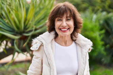 Orta yaşlı bir kadın parkta kendine güvenerek gülümsüyor.