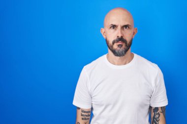 Mavi arka planda duran İspanyol dövmeli adam yüzünde ciddi bir ifadeyle rahatlamış. Basit ve doğal bir şekilde kameraya bakıyorsun.. 