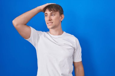 Mavi arka planda duran beyaz tenli sarışın adam. Kendine güvenen, el hareketleriyle saçlara dokunan, çekici ve modaya uygun poz veren. 