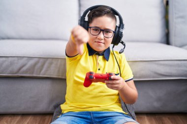 Kulaklık takmış, bilgisayar oyunu oynayan, mutsuz, reddedilmiş ve olumsuz jestler yapan İspanyol bir çocuk. kötü ifade. 