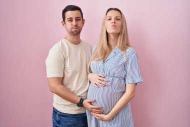 Genç bir çift pembe arka planda durup komik suratlı yanakları şişiren bir bebek bekliyor. Havayla şişmiş ağız, çılgın bir ifade.. 