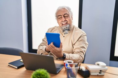 Ofiste dokunmatik ped ve dizüstü bilgisayar kullanan orta yaşlı, kır saçlı bir iş adamı.
