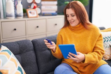 Young beautiful plus size woman using touchpad and credit card sitting on floor at home