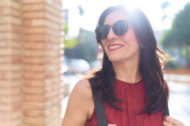 Orta yaşlı İspanyol kadın gülümsüyor. Kendinden emin bir şekilde caddeye bakıyor.