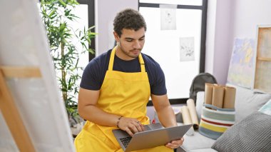 Sarı önlüklü genç bir adam modern bir sanat stüdyosunda dizüstü bilgisayar kullanıyor. Yaratıcılık ve eğitimi gösteriyor..