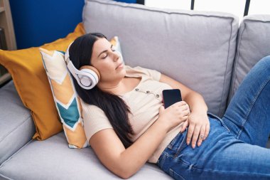 Genç, güzel İspanyol kadın evdeki kanepede müzik dinliyor.