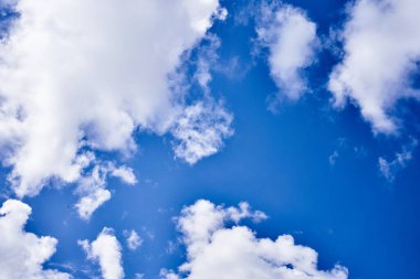 Uçsuz bucaksız mavi gökyüzü kabarık beyaz bulutlar ve yüksekte süzülen küçük bir uçakla süslenmiş..