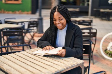 Kahve dükkanının terasında kitap okuyan Afrikalı Amerikalı kadın.